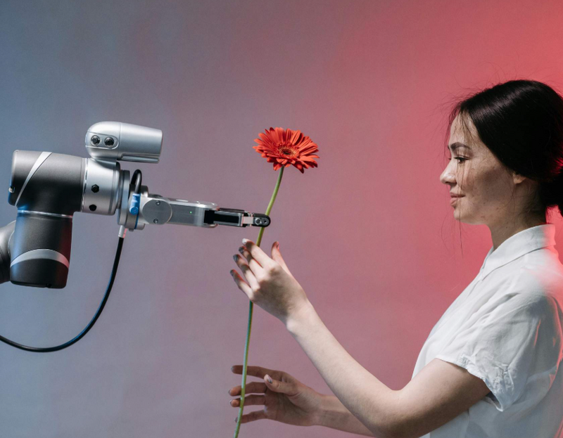 Ein robotischer Greifarm übergibt einer jungen Frau eine rote Blume