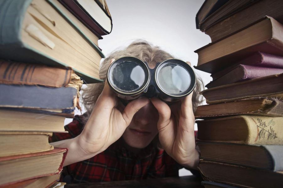 Junge mit Fernglas zwischen zwei Stapel von Büchern als Symbol für eine zentrale Enterprise Suche