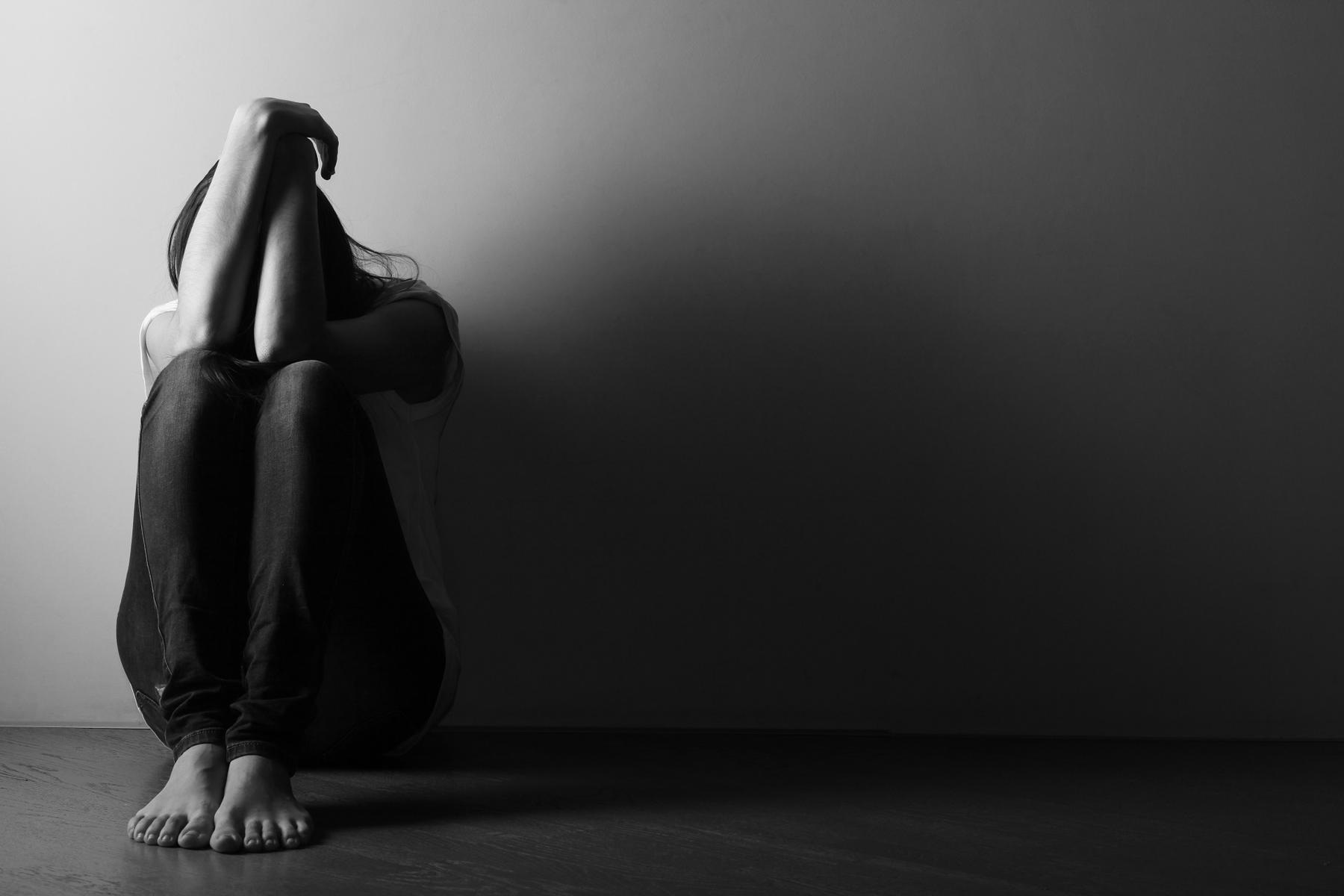 Eine junge Frau mit Depression sitzt auf dem Boden mit verschränkten Armen über dem Kopf