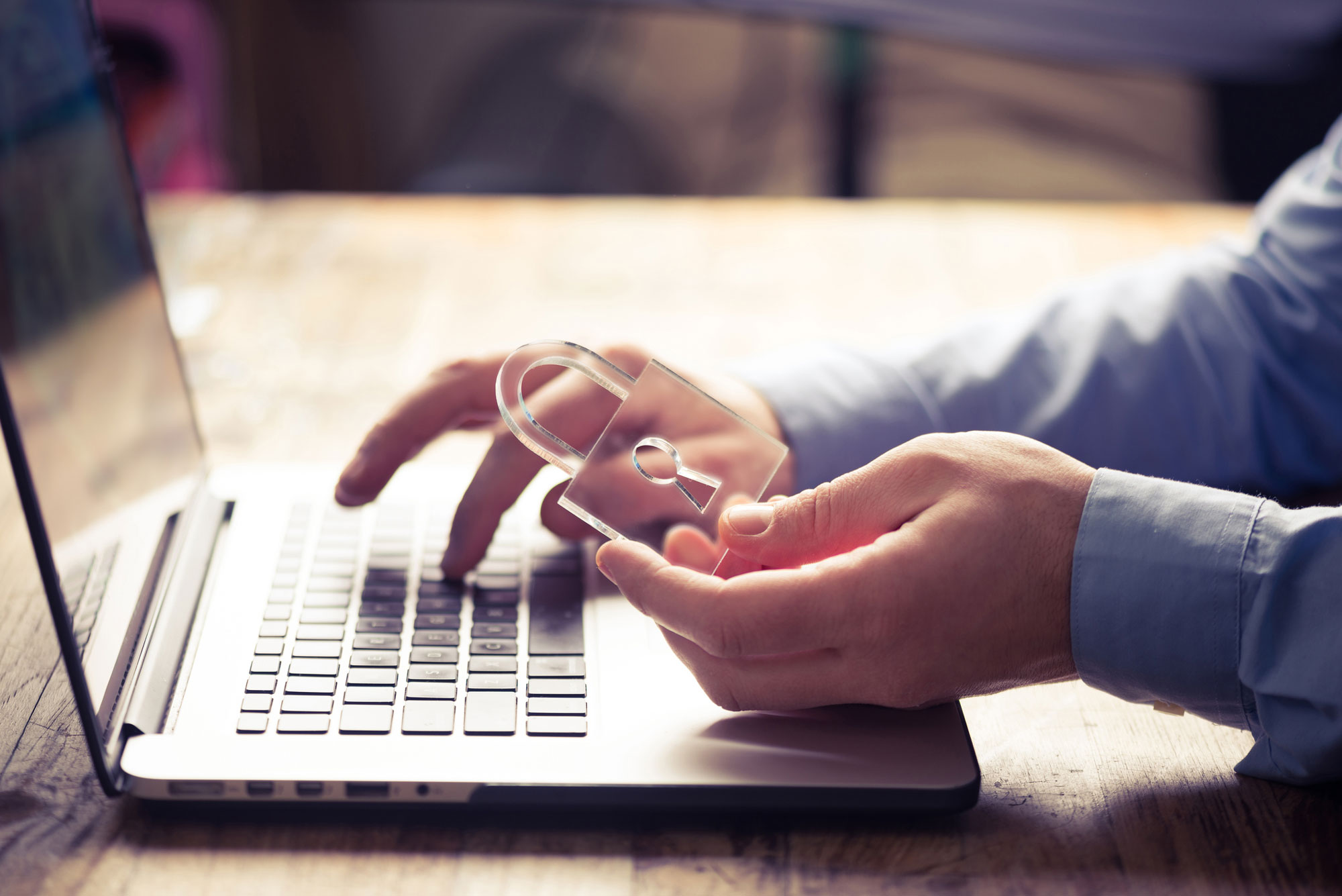 Person hält ein Schloss in der linken Hand über die Tastatur eines Laptops