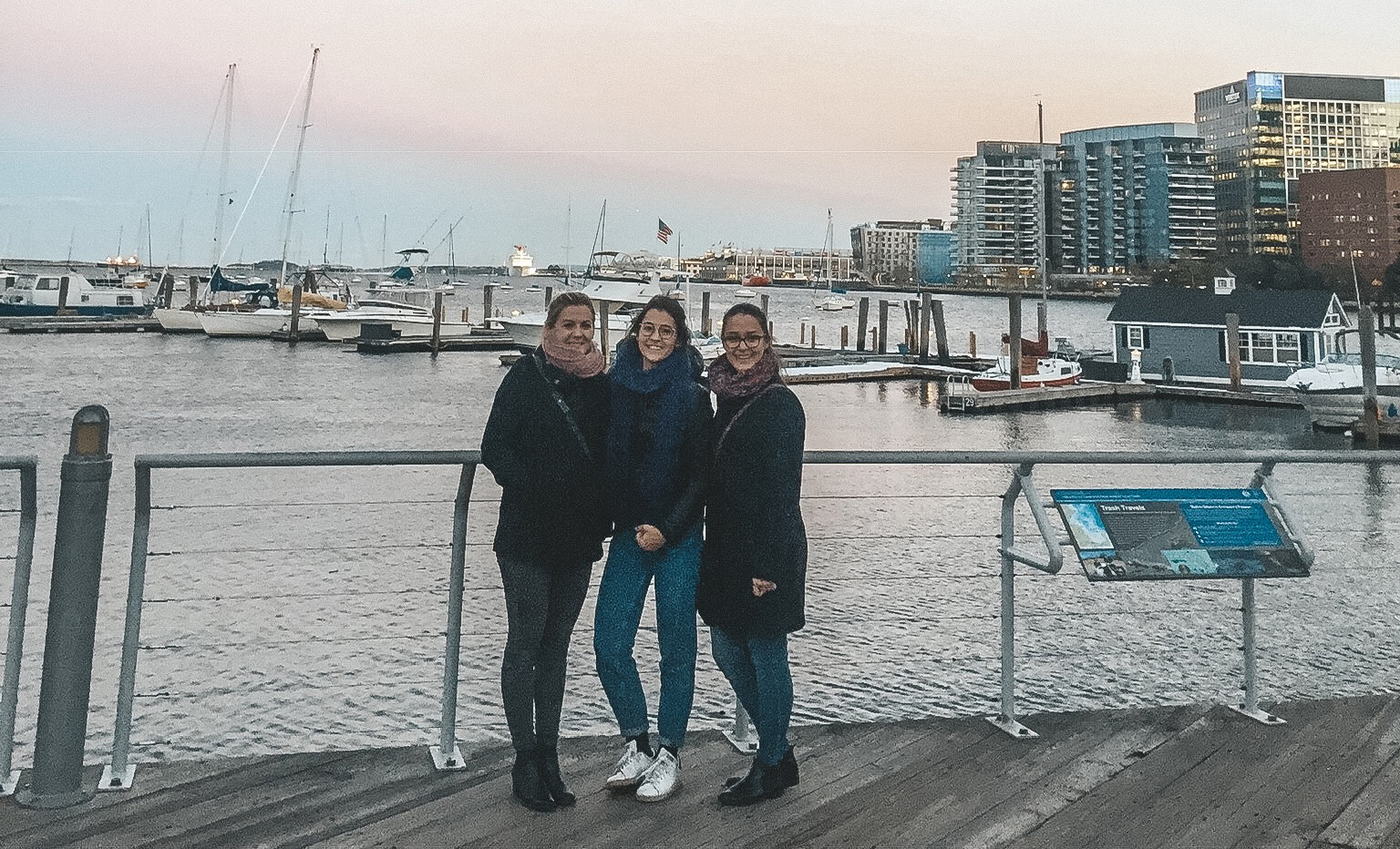 Drei Doktoranden vor einem Gelände, im Hintergrund ein kleiner Pier auf das Meer