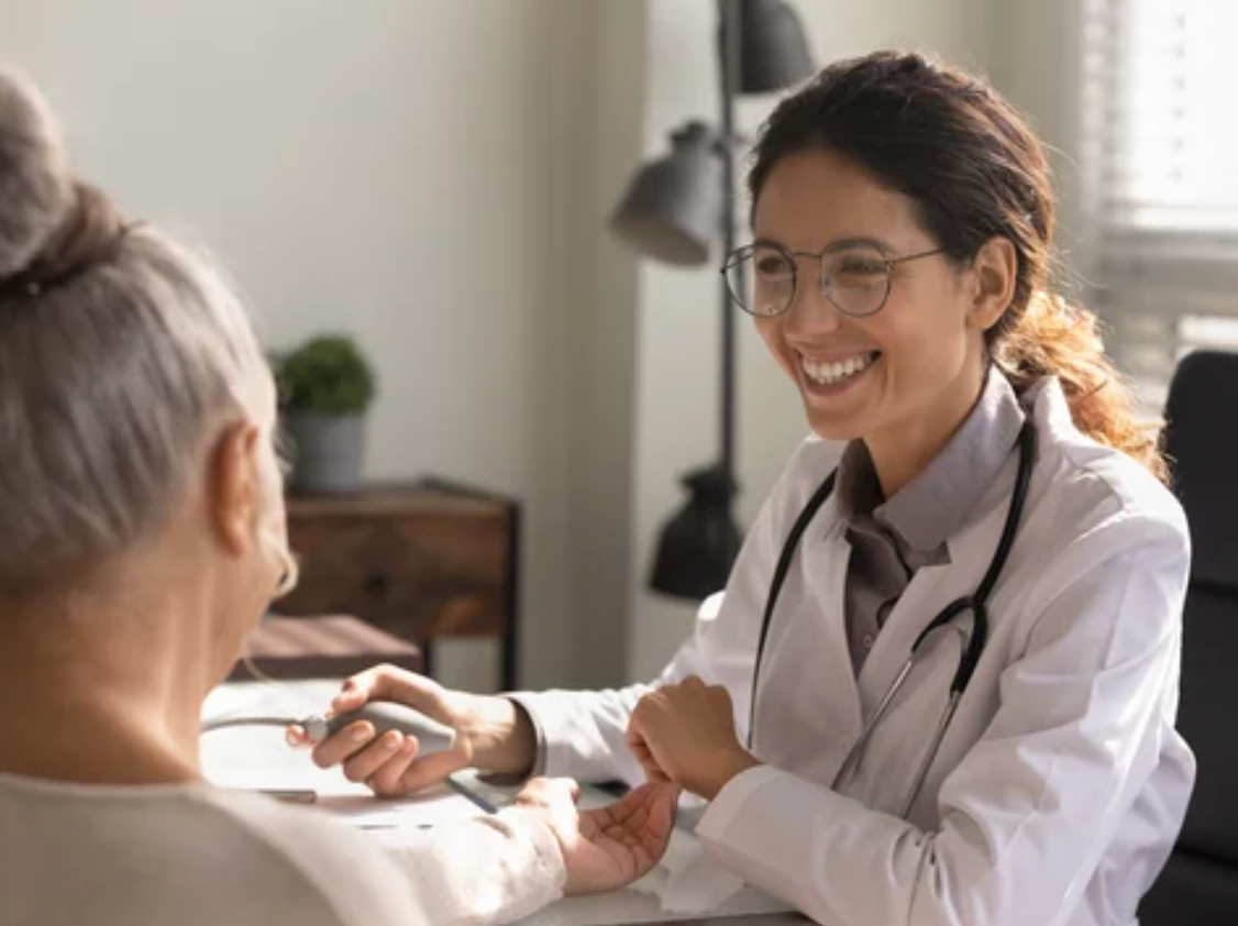 Eine Ärztin hält lächelnd die Hand einer älteren Patientin