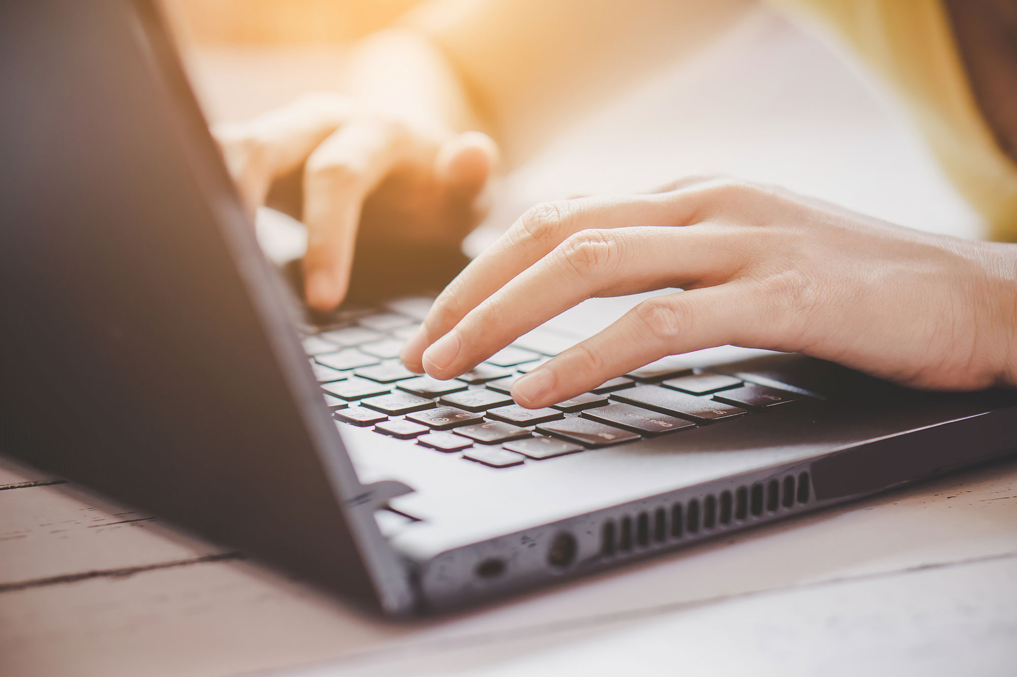 Person sitzt vor einem Laptop und tippt