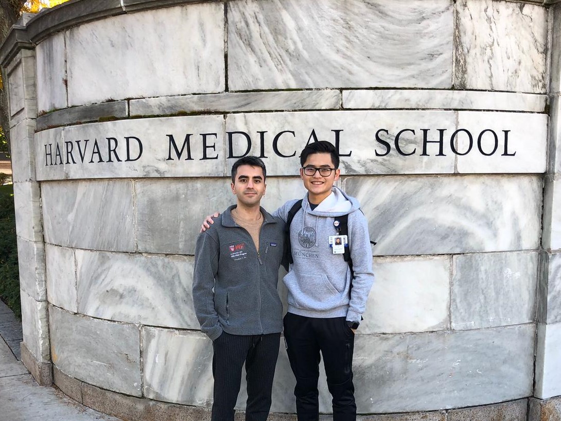 2 Doktoranden vor einer Steinmauer auf der "Harvard Medical School" steht